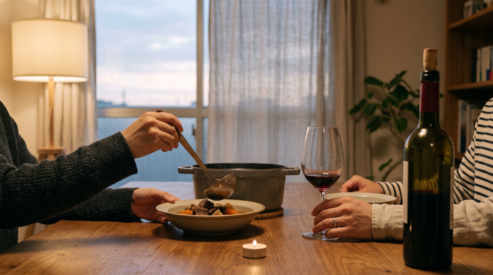 夕方の食卓で煮込み料理を器によそう手と、少量の赤ワインが入ったグラスに添えた手、開けたボトル
